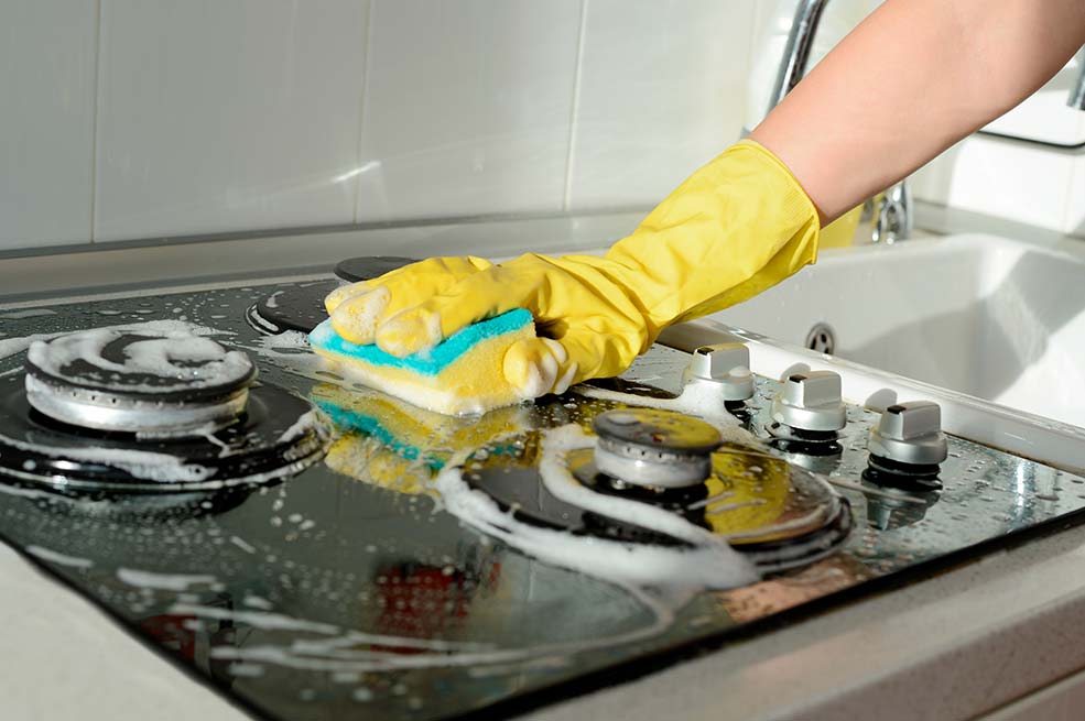 person wearing yellow rubber gloves and cleaning a stovetop with a sponge