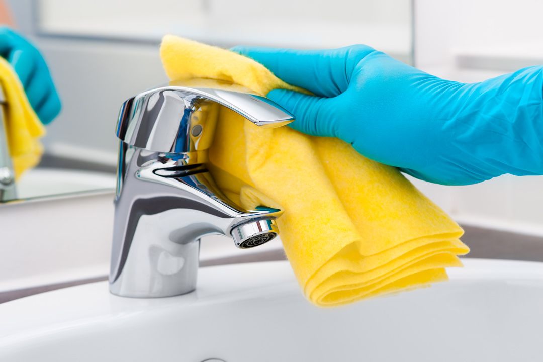 hand cleaning a bathroom faucet with a yellow cloth