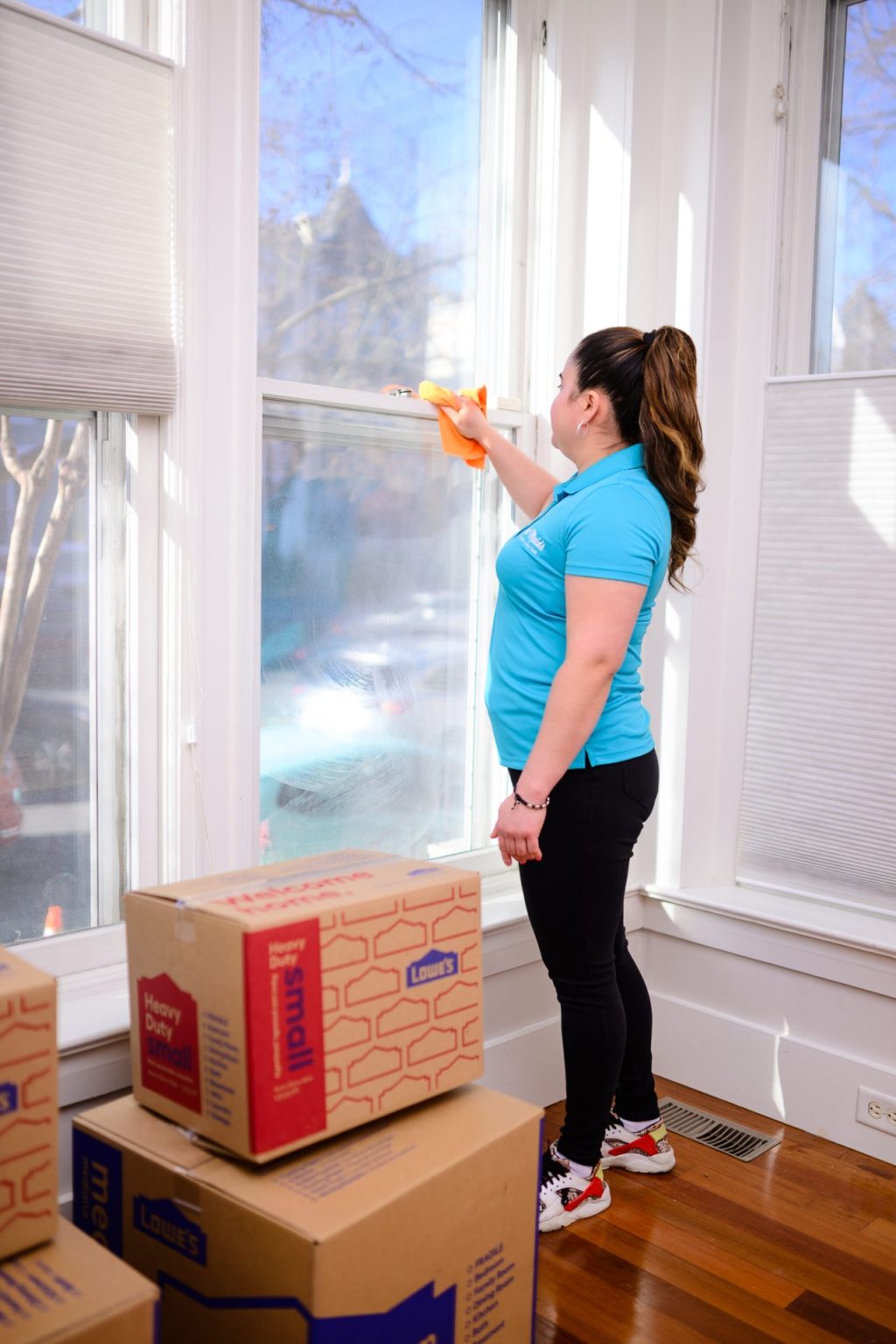 Rent Maids cleaner wiping a window frame in an empty room with moving boxes